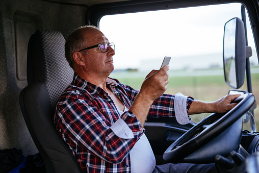 Male trucker driving a semi and texting on a mobile phone.