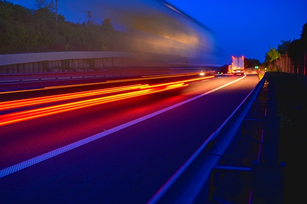 Blurred image of trucks and cars driving at night on a highway with red tail lights creating light trails.
