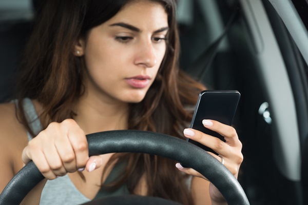 Driver looking at a cellphone while holding the steering wheel, showing how distracted driving increases crash risk and can impact liability in car accident claims.