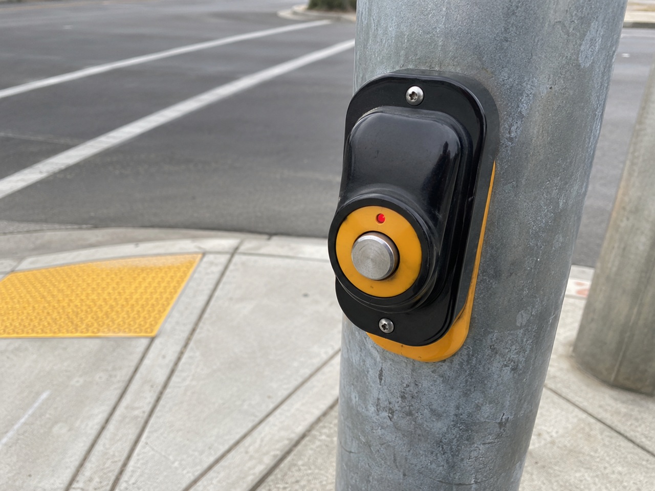 A close-up of a pedestrian crossing signal button with an illuminated red indicator light mounted on a metal pole at a city crosswalk with a yellow tactile paving pad, representing municipal pedestrian safety infrastructure, rising traffic fatalities, and pedestrian accident injury claims in Jacksonville, Florida.